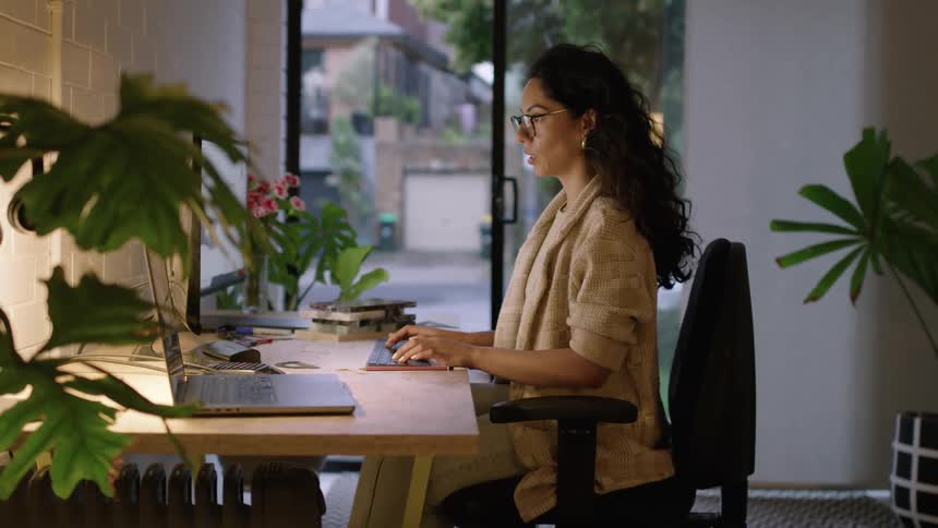 A woman is sitting at a desk in an office typing on a computer