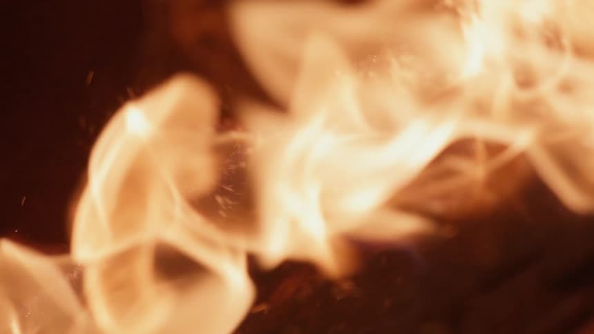 Extreme close up of orange yellow flames washing over a metallic chain on the ground