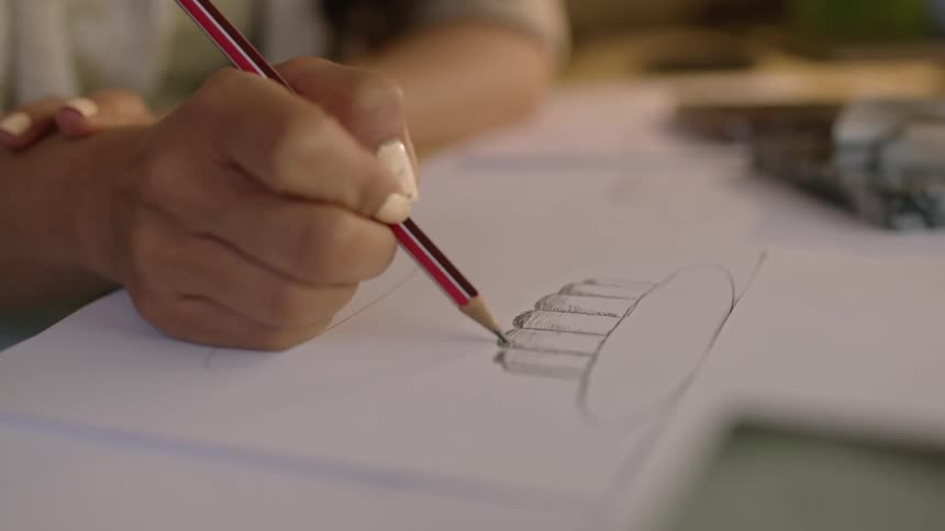The hand of a child is shown drawing a cupcake on paper with a pencil