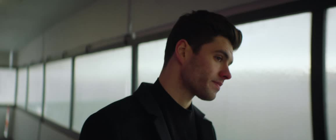 Young sad man wearing black walks on a corridor and reclines on the window