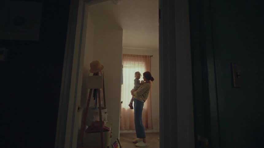 A mother holds her child in their bedroom in front of a window