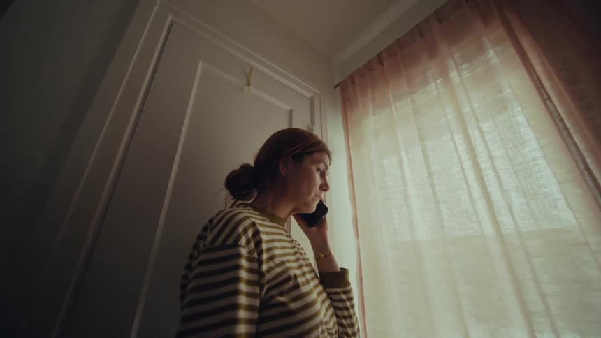 A woman talking on the phone standing in front of a window