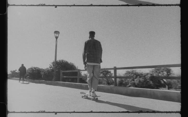 A young man is skateboarding on a boardwalk while others are walking along on a bright sunny day