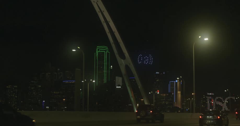 Traffic moves across a bridge to a city with tall buildings and skyscrapers lit up at night