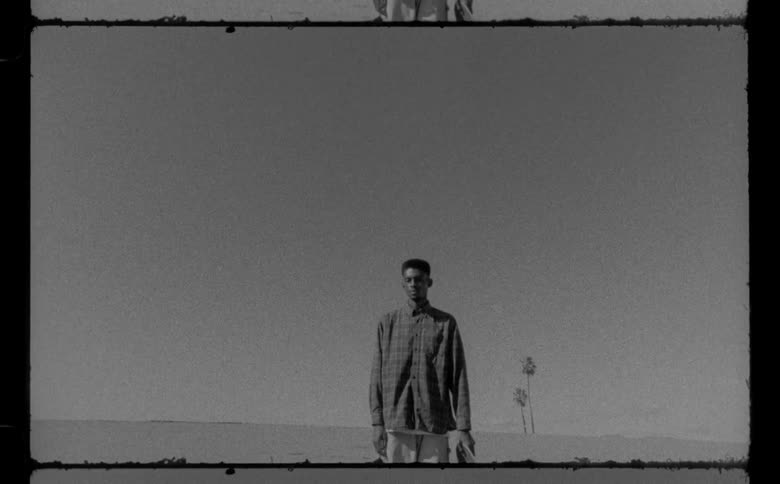 A zoom in of a man standing at the edge of a court with skateboard in his hands
