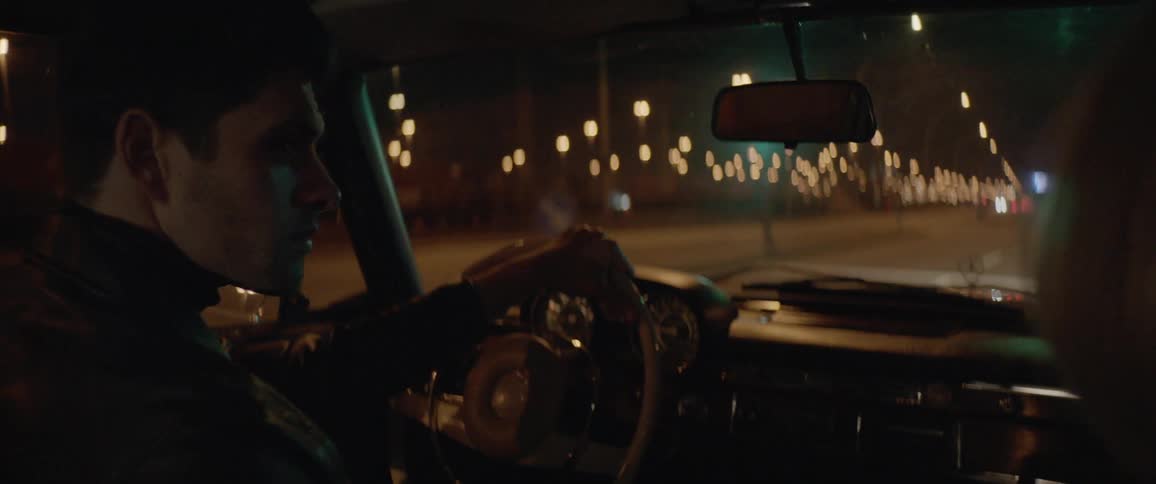 Young fashionable couple on a vintage car driving in the city street at night