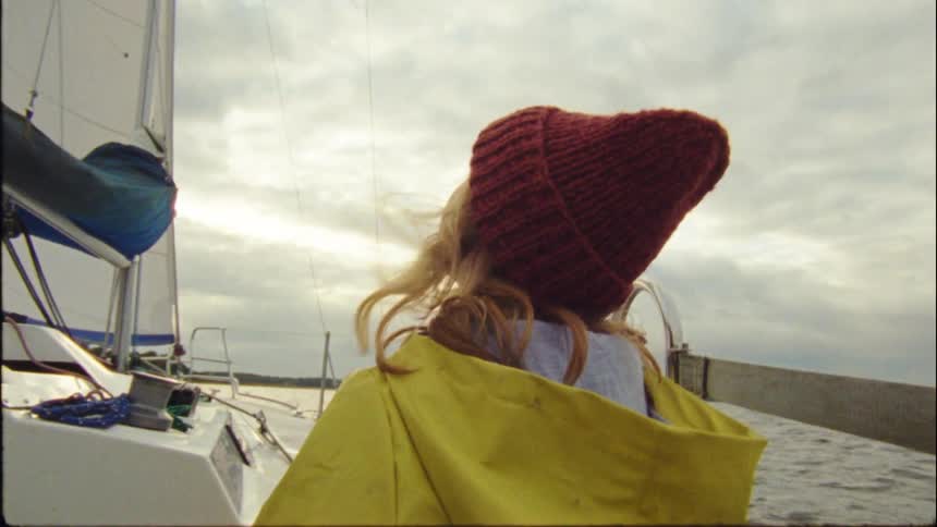 A person in a yellow coat and red hat looks up at the sky while on a boat