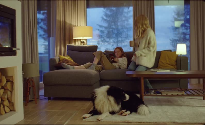 Dog sits up as mother walk into room to sit next to where daughters is reading on a rainy day