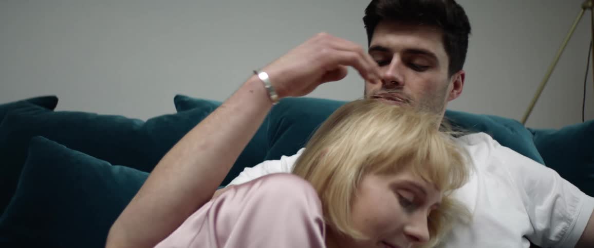 Couple cuddles together on couch as man strokes the hair of the woman