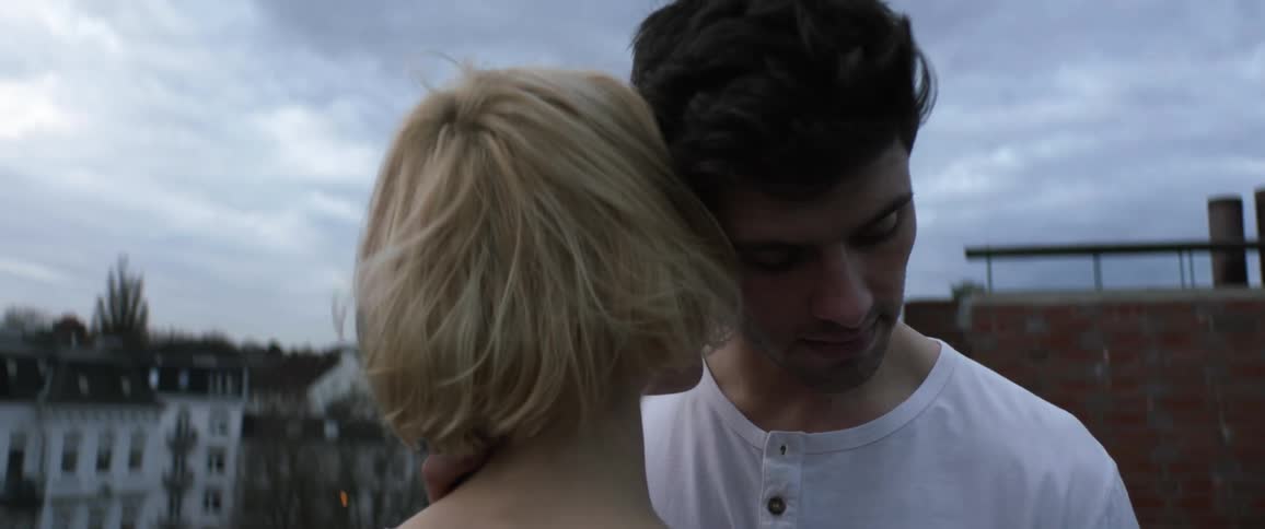 A man and woman nuzzling each others faces on top of a building