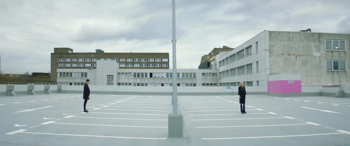 Two people standing in an empty parking lot on opposite sides of each other