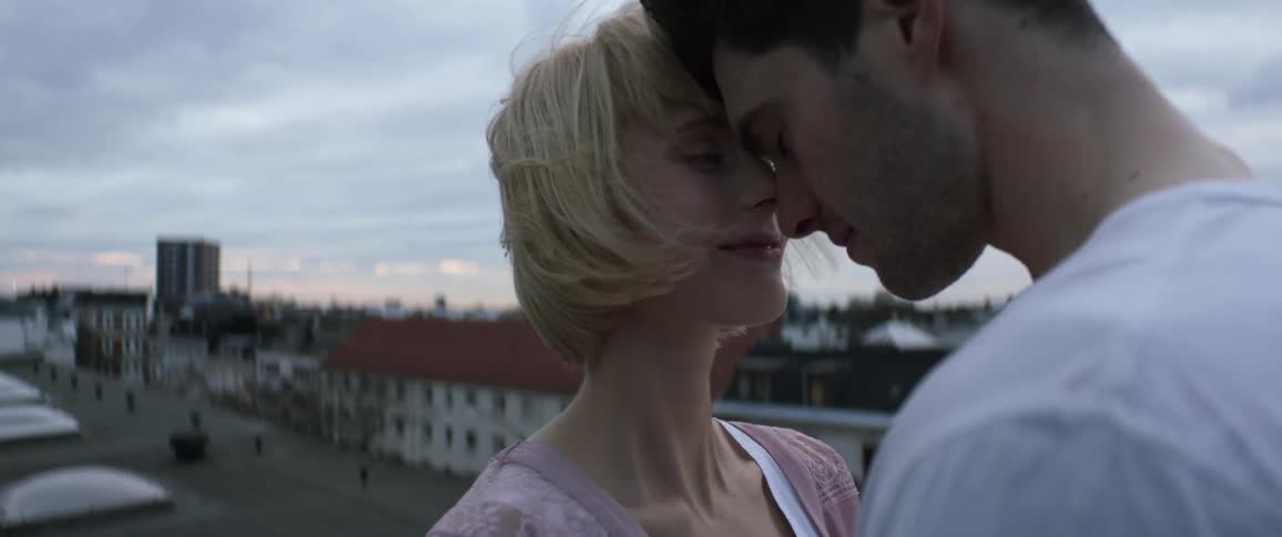 Young couple in love touch foreheads and kiss while standing atop a building in the morning