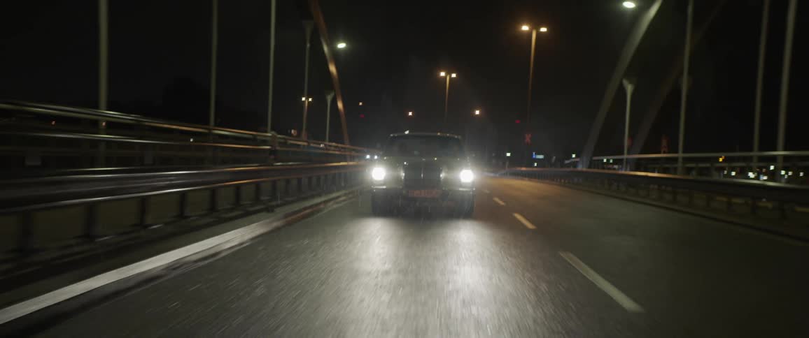 Two people sit in car crossing bridge at night