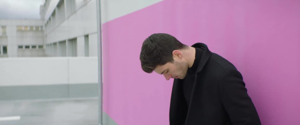 Young man wearing black clothes modeling in front of a pink wall on a parking garage