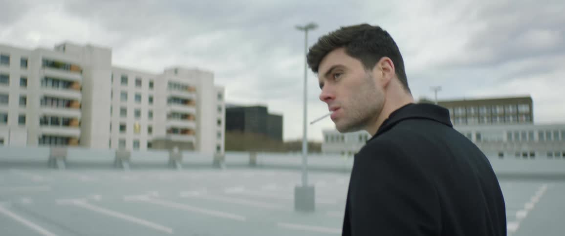 Man lights cigarette and smokes while walking across rooftop parking lot