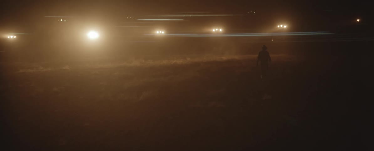 Cowboy walks across foggy pasture at night following loose horse