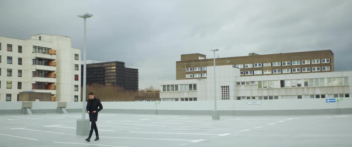Man walks across empty rooftop parking lot near apartment buildings on an overcast day