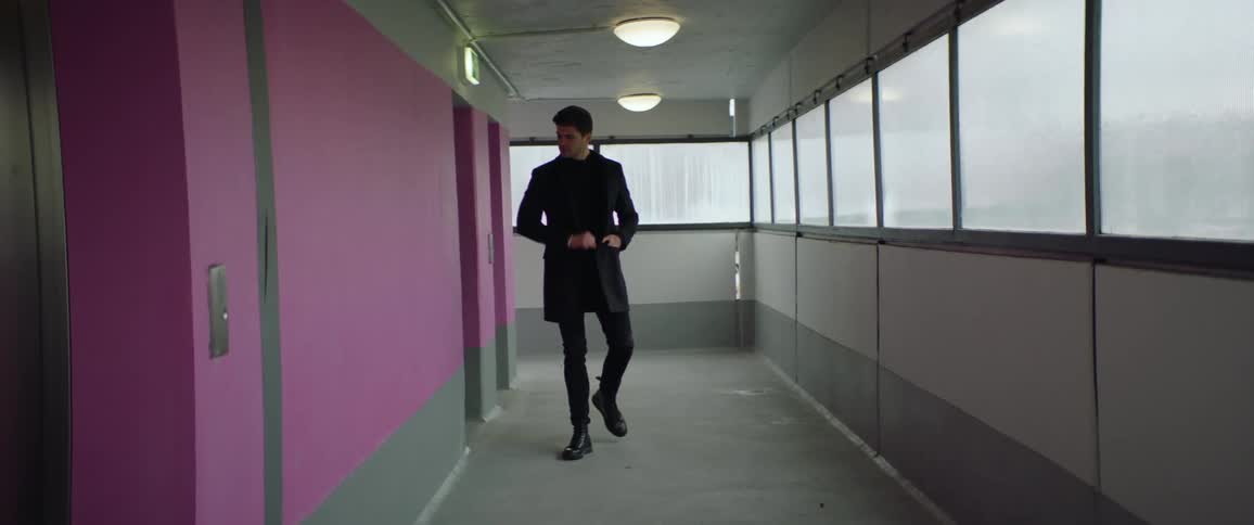 Man wearing black coat and pants pounds on pink wall in the office