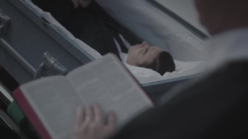 A person is holding a book before a casket