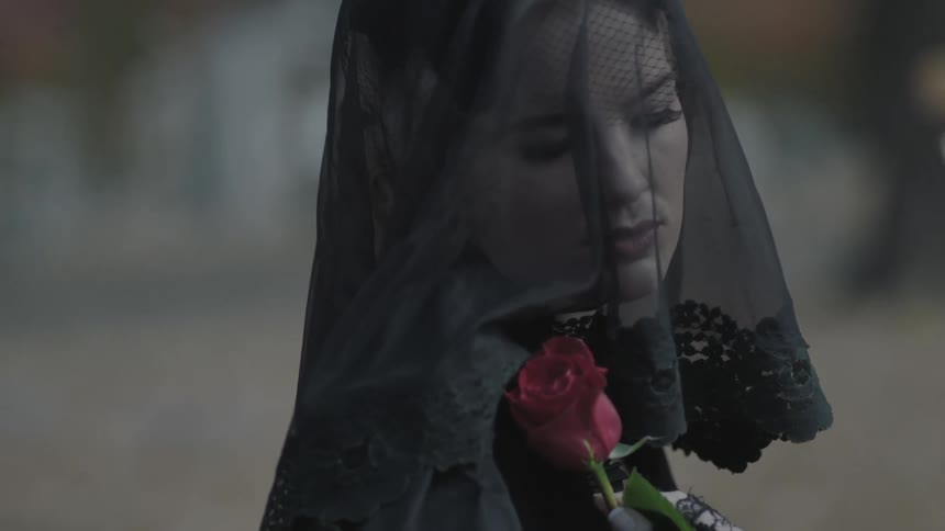 A woman wearing a black veil is holding a red rose