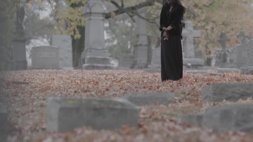 Woman in black stands mourning in a cemetery