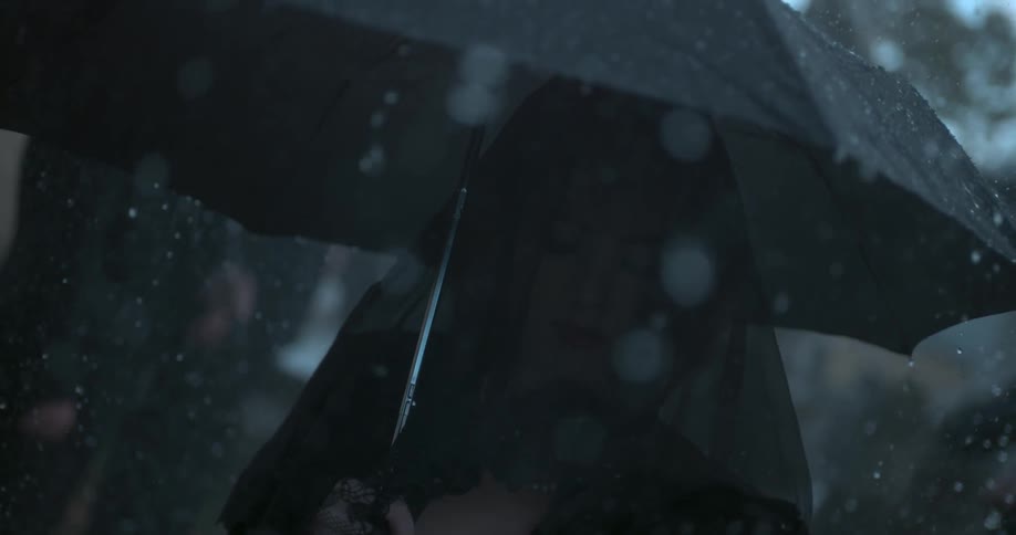 A veiled woman walks in the rain with an umbrella