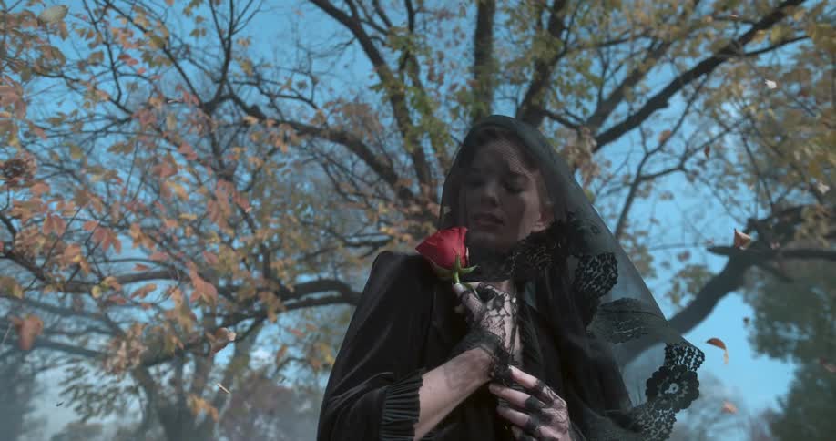 A woman in black holds a rose under a tree