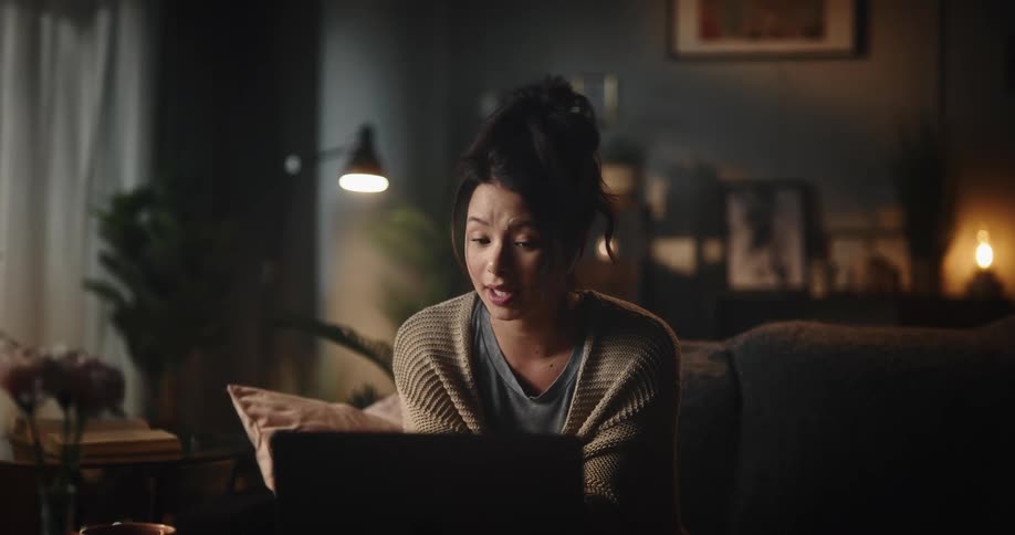 A woman uses her laptop for a video call while sitting on a couch at home
