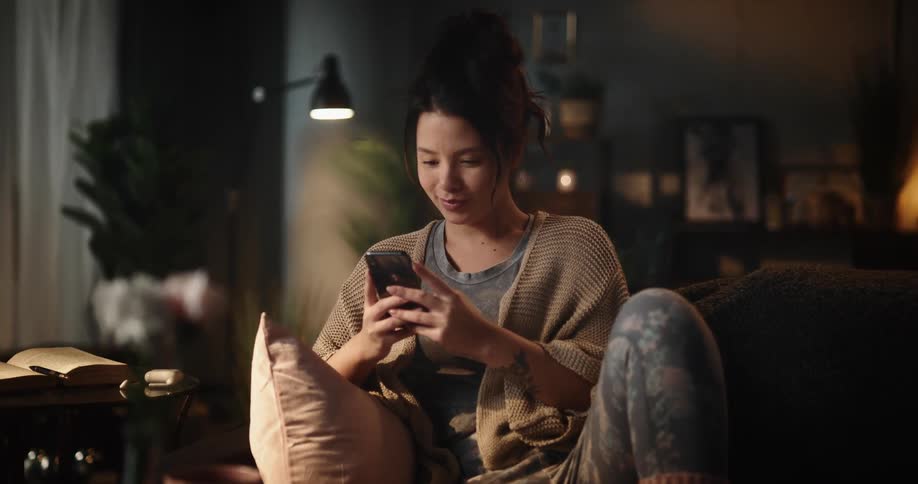 Woman sitting on couch smiles while interacting with smartphone