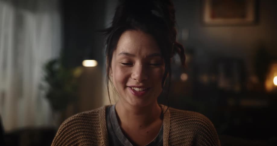 A woman smiling while looking at a smartphone in a living room