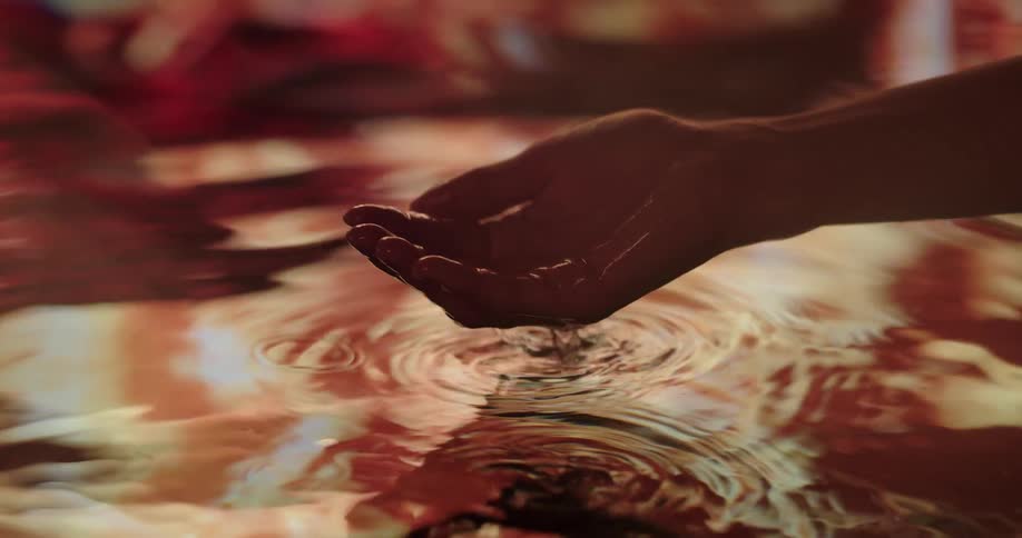A persons hand scooping up water creating ripples as it reflects