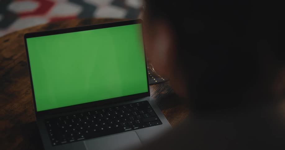 A woman at home taps a button on her laptop with a green screen