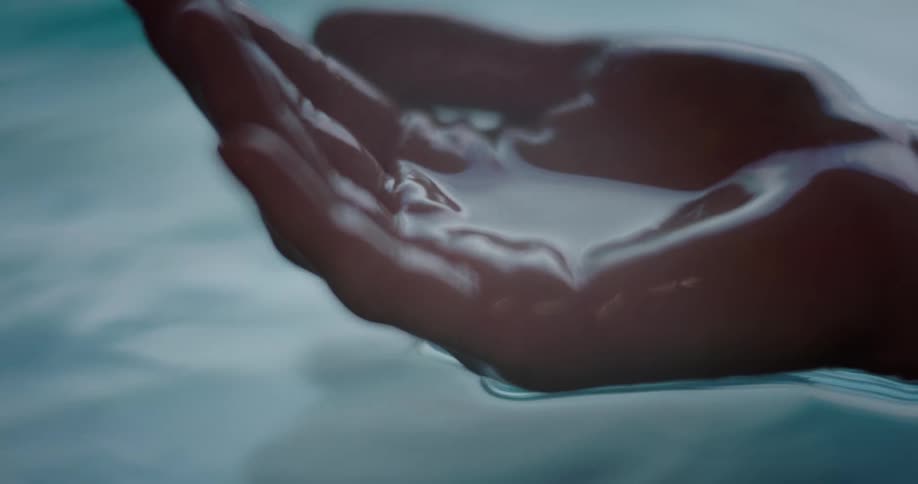 One hand slowly dips into water and lifts out a handful of water and releases it