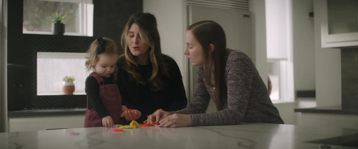 Two adult women playing with a little girl at the kitchen counter