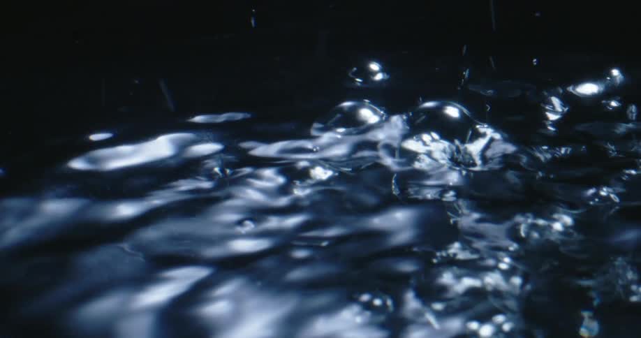 Rain falls onto water creating bubbles and ripples