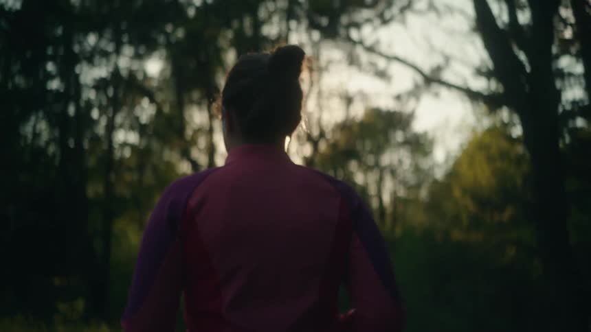 A woman stands looking as the sun shines brightly through the trees in the woods