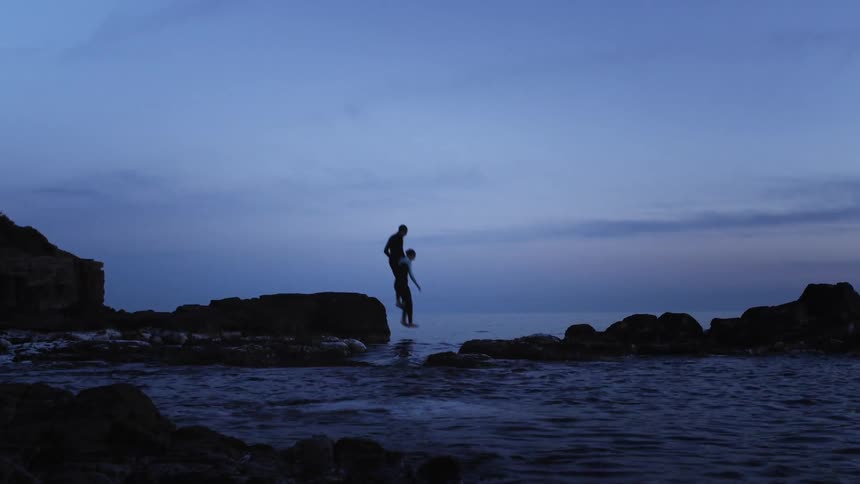 Two men jump into the ocean from off a small cliff