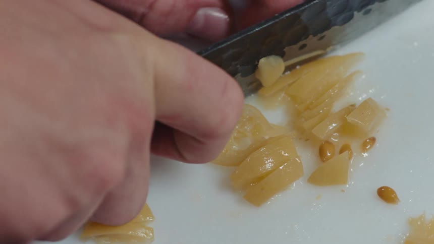A perons hands using a knife to cut food on a white cutting board