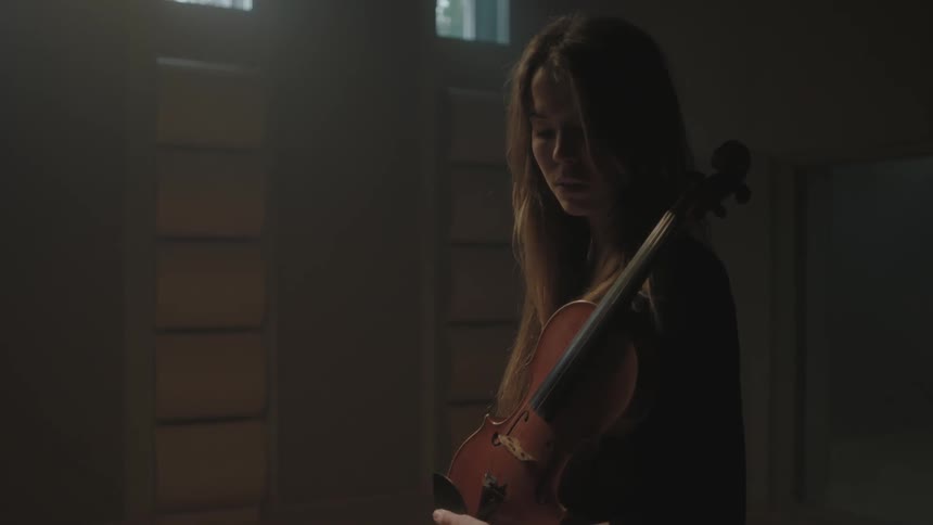 A woman is holding a violin in a dark room