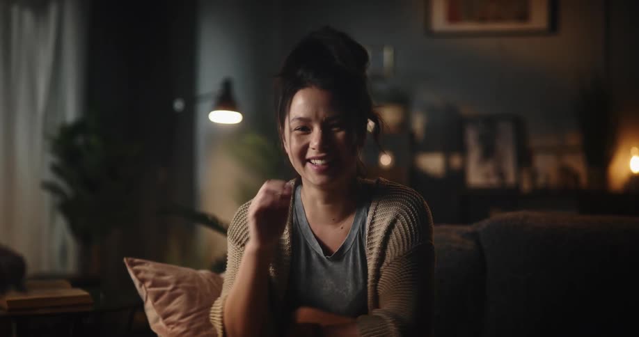 Happy woman waves goodbye on a video call through her laptop in the living room at home and then looking at the camera