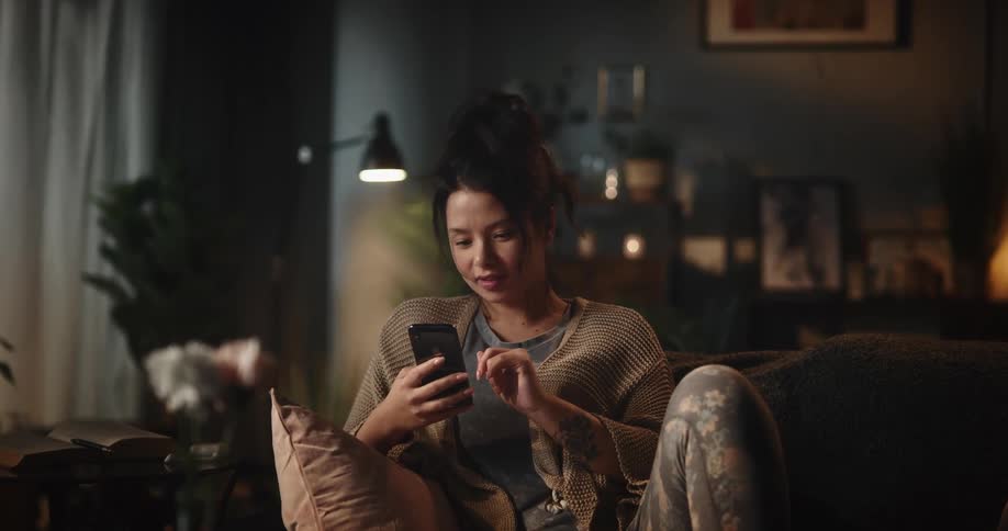 A woman uses a smartphone while sitting on a sofa in a living room