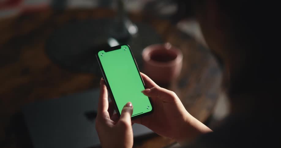A woman at home taps on a green screen on her cell phone