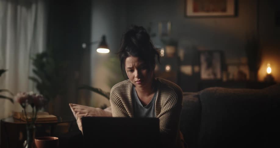 Young woman having a serious discussion on zoom on laptop while sitting on couch in living room