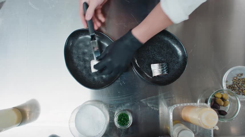 Top down view of a chef plating a dish of raw fish on a restaurant kitchen