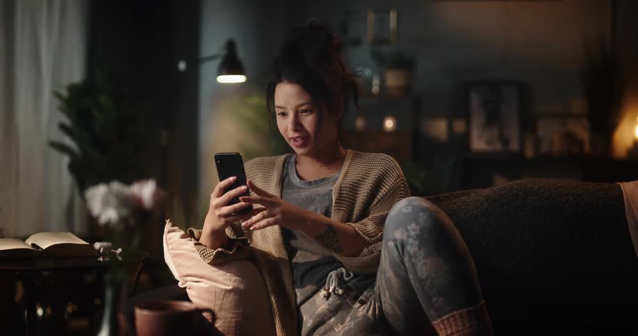 A woman walking to her couch siting down and talking to someone on her phone via face chat