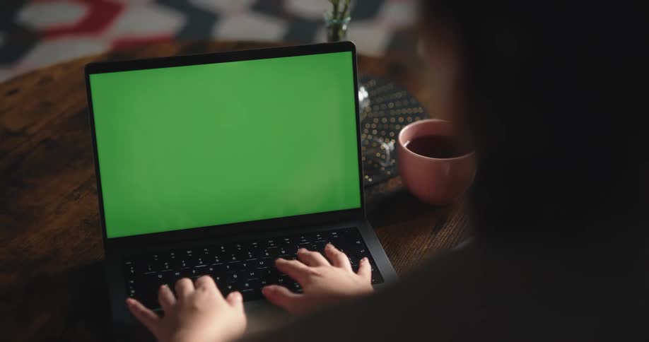 Woman sits at small wooden table typing on a laptop