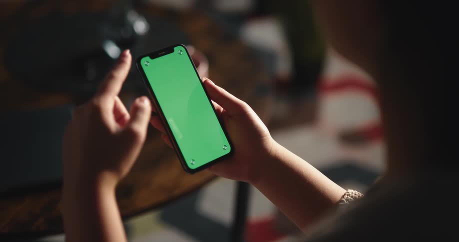 Woman sits near wooden table scrolling on smartphone