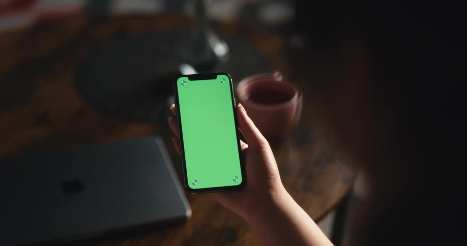 A person looks at the screen of a smartphone while sitting at a table indoors