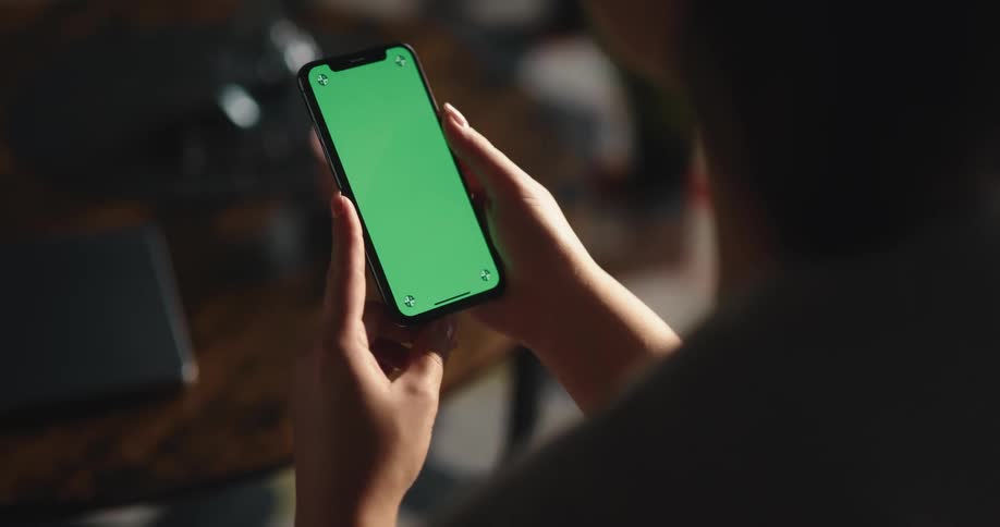 Woman holding a smartphone with replaceable green screen swipes up left and right