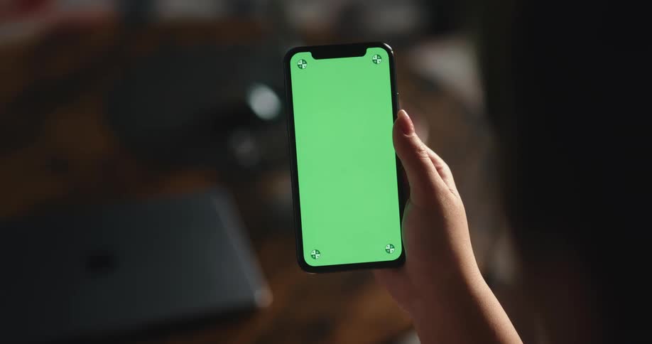A persons fingers holding a phone with a green screen on it